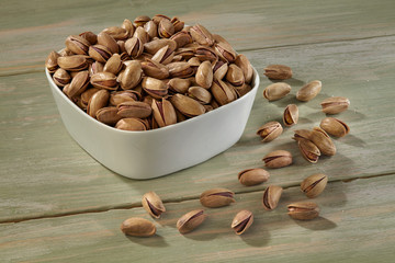 Pistachios in white bowl on wooden background