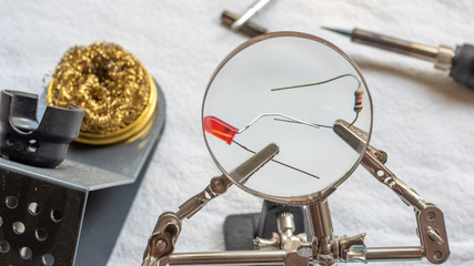 Soldering a resistor and LED with a magnifying glass, with alligator clips holding the components