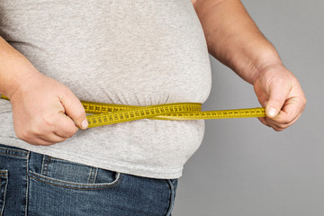 A man measures his fat belly with a measuring tape. on a gray background.