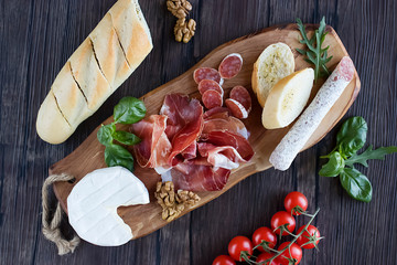 Prosciutto, bread, olives, walnut, mozzarella, salami, basil and cherry tomatoes on  brown wooden board.  Mediterranean kitchen. Top view.