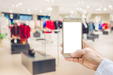 Mockup image of man hand holding gold mobile phone with blank white screen on blurred abstract background of many cotton clothing on the shelves of fashion shop.business concept.shopping online.