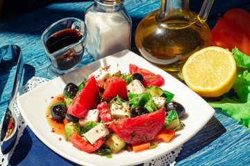 Vegetable salad in bowl on blue wooden table. Tasty greek salad with feta, olives and tomatoes in a bowl. bright daylight shot. Traditional greek salad with fresh vegetables, feta cheese and olives.