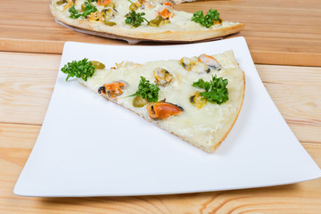 Slice of cooked pizza with mussels on a square dish