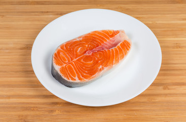 Uncooked steak of arctic char on dish on wooden surface