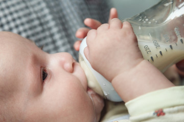 Baby drinking milk from glass bottle holding by father. Healthy nutrition