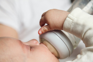 Baby drinking milk from glass bottle holding by father. Healthy nutrition