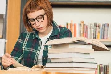 Young redhead woman in glasses read book in the library