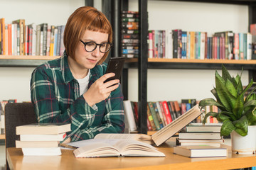 Young redhead woman in glasses read book in the library