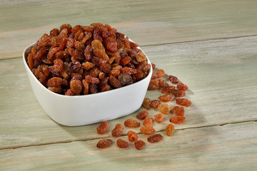 Raisins in white bowl on wooden background