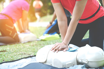 Obraz na płótnie Canvas Asian female or runner woman training CPR demonstrating class in park by put hands and interlock finger over CPR doll give chest compression. First aid training for heart attack people or lifesaver.