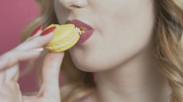 girl eating an appetizing macaroon on a colored background, a young woman bites a cookie and it crumbles, diet concept, food industry