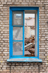 Window with a blue frame in the wall of the destroyed house with fragments of brickwork indoors. Dismantling of buildings.