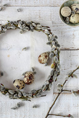 Quail eggs and pussy willow wreath as a symbols of spring and Easter on a white wooden background