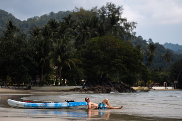 Happy young man lying near a kayak boat on Ko Chang, Thailand in April, 2018 - Best travel destination for happiness