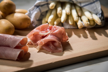 Roher, weißer Spargel in Tuch mit Kochschinken, geräucherten Schinken und Kartoffeln auf Holz Brett und Marmor Hintergrund