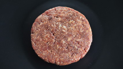 Round burger cutter rotates around its axis on an isolated black background, cutlet from beef or veal, top view