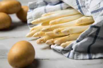 Roher, weißer Spargel in Tuch und Kartoffeln auf Marmor Hintergrund