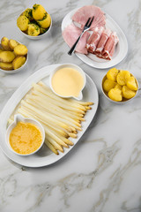 Platte weißer Spargel mit Sauce Hollandaise, zerlassener Butter, Kochschinken, geräucherten Schinken und Kartoffeln auf Marmor Hintergrund