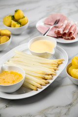 Platte weißer Spargel mit Sauce Hollandaise, zerlassener Butter, Kochschinken, geräucherten Schinken und Kartoffeln auf Marmor Hintergrund