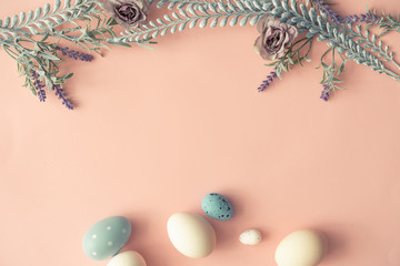 Creative layout made with spring flowers leaves and Easter eggs on pastel pink background. Minimal nature composition.