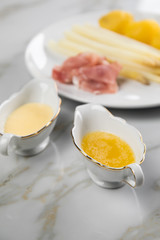Weißer Spargel mit Sauce Hollandaise, zerlassener Butter, geräucherter Schinken und Kartoffeln auf Teller und Marmor Hintergrund