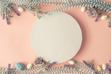 Creative layout made with spring flowers leaves and Easter eggs on pastel pink background. Minimal nature composition with paper card copy space.