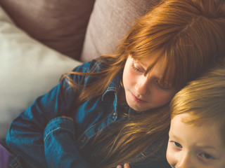 Two blonde little kids in blue on gray sofa