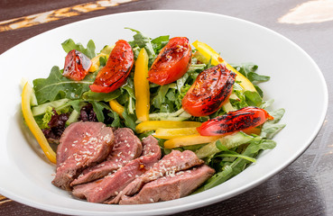 Salad with roast beef and sun-dried tomatoes on dark background
