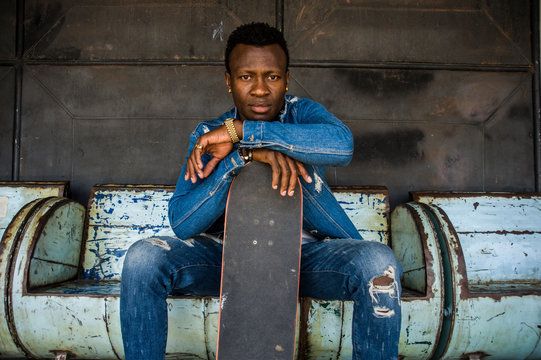 young handsome and attractive black African American skateboarder man sitting on city grunge bench holding skate board posing in cool attitude