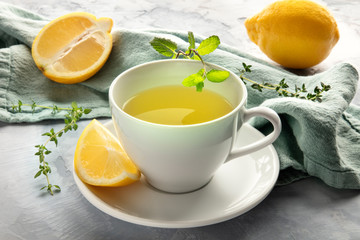 A closeup of a cup of green tea with lemons and herbs