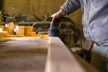 Carpenter works in the workshop of processing wooden boards, grinding machine, sander in the hands of a worker