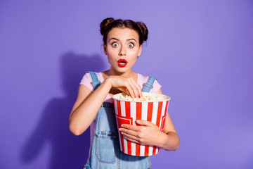 Close up photo beautiful amazing she her lady two buns watch tv show hold popcorn bucket eyes full fear mouth open wear casual t-shirt jeans denim overalls clothes isolated purple violet background - obrazy, fototapety, plakaty