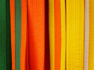Fototapeta premium Closeup of martial arts belts for karate or kickboxing - white with yellow tag, yellow, yellow with orange tag, orange, orange with green tag, green