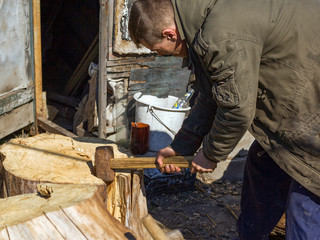 a young guy in the village chopping oak stumps with a wedge and sledgehammer, harvesting wood