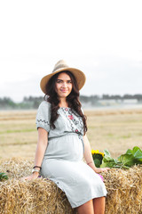 lovely pregnant woman next to the hay bale in the sunlight