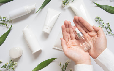 Serum or essential oil w/ organic herbal extract. Woman's hand holding vial w/ dropper and natural skincare bottles on white background. Natural beauty cosmetic product. Top view. Copy space. - obrazy, fototapety, plakaty