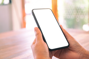 Mockup image of woman's hands holding black mobile phone with blank white screen on wooden table