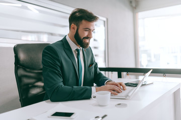 Happy Caucasian bearded businessman in formal wear using laptop in office. A winner is a dreamer who never quits.