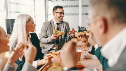 Small group of happy colleagues in formal wear chatting and eating pizza together for lunch. Great...