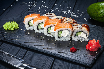 Set of fresh sushi rolls with salmon and eel on dark stone served with ginger and wasabi and wooden black wooden table. Japanese cuisine. Copy space. Served sushi for menu
