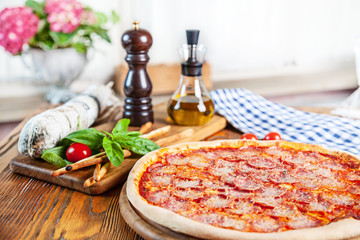 Selective focus on pizza with salami and tomato. Fresh homemade pizza with ingridients on background: salami, basil, cherry tomato, olive oil. Image with copy space for desig or logo. Italian cuisine