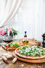Close up view on fresh served pizza with prosciutto on a wooden table on light background. Pizza with wine. Vertical image with copy space for text. Food for menu. Italian cuisine. 