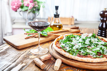 Close up view on fresh served pizza with prosciutto on a wooden table on light background. Pizza with wine. Vertical image with copy space for text. Food for menu. Italian cuisine. 