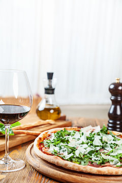 Close up view on fresh served pizza with prosciutto on a wooden table on light background. Pizza with wine. Vertical image with copy space for text. Food for menu. Italian cuisine. 