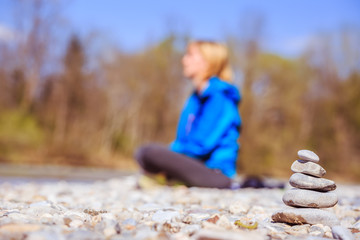 Meditation and relaxation: Cairn in the foreground, meditating woman in the blurry background. Enjoying the summer.