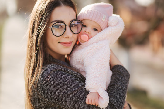 Portrait of mother and her little baby girl. Beautiful mom and cute baby. Mother hud her daughter. Baby dressed in peanch colour hat and nipple toy