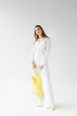 pretty young woman holding yellow string bag with baguette and bottle of milk on white