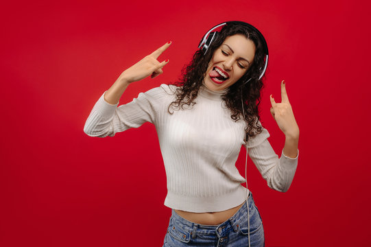 Beautiful rocking girl, showing tongue, with headphones and closed eyes,  isolated on red background