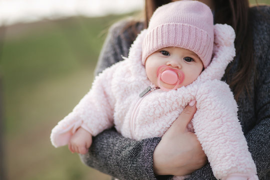 Little baby girl on mother's hands in pink clothes. Cute baby with peanch colour nipple toy