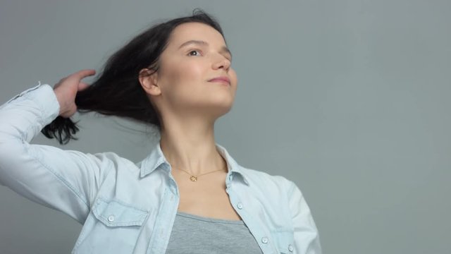 Brunette in studio portrait video shoot wwears jeans shirt with blowing hair slow motion from 60 fps Calm brunette portrait watching aside, touches her hair and then turns to the camera